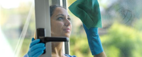 Young woman cleaning windows at home, she is wiping glasses
