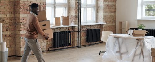 Young Afro-American employee in sweater bringing stack of moving boxes in office during relocation